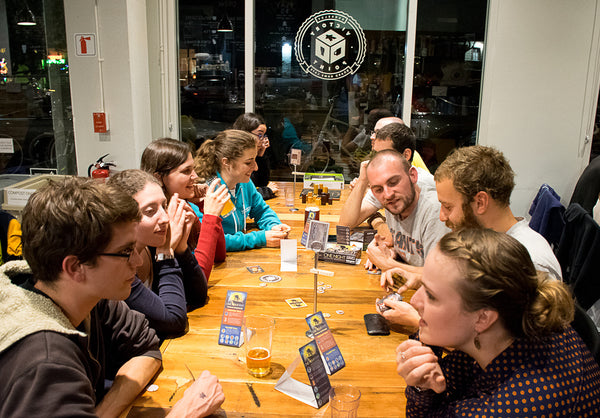 Friends gathered at a long table playing a party game.